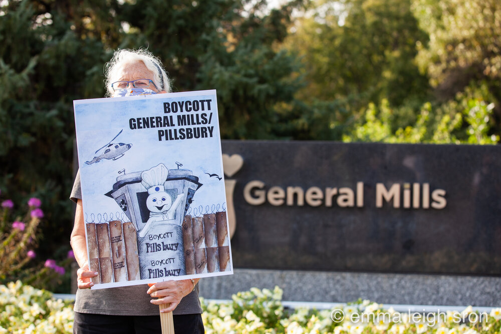 A protest sign at General Mills headquarters, Minneapolis, shows a Pillsbury Doughboy waving from an Israeli military watchtower. Photo: Emma Sron. More photos at emmasron.com
